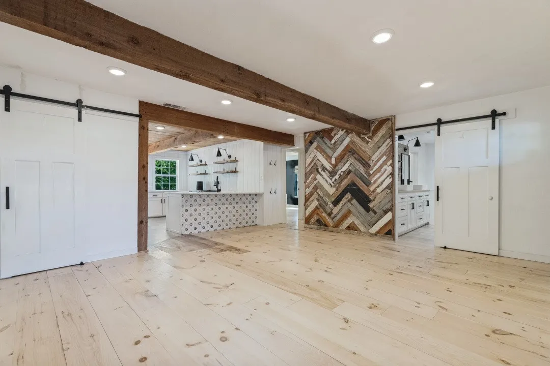 Light wood-finish flooring, exposed wood beams, and a chevron-pattern accent wall