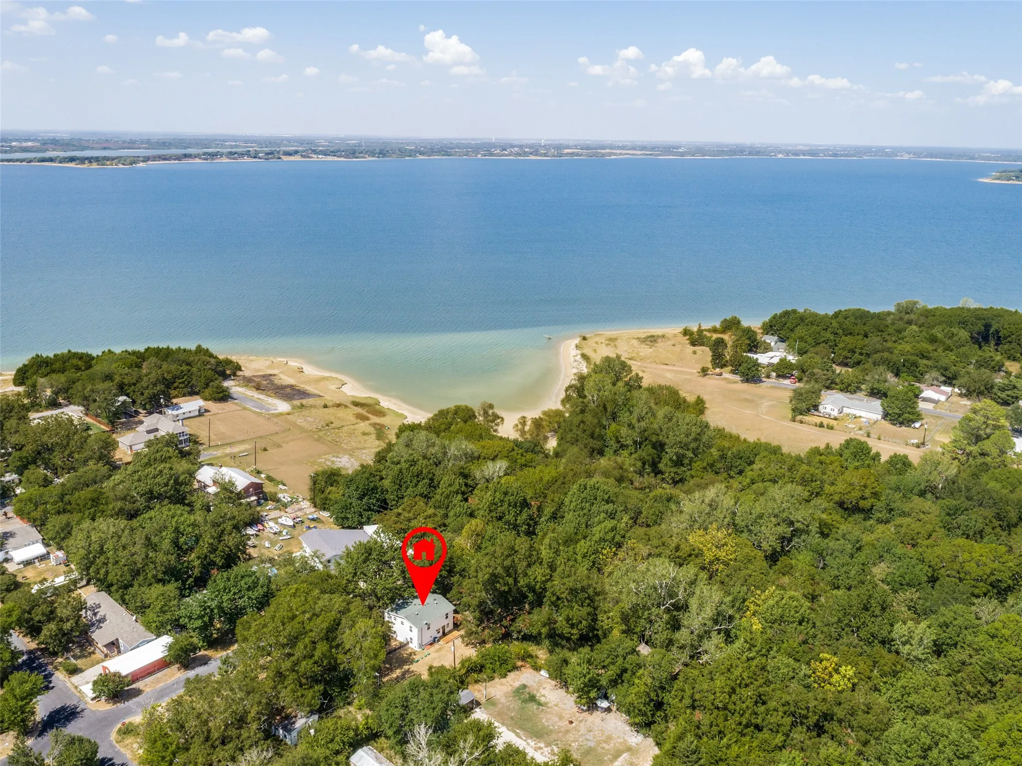 Lakefront property with direct access to a natural beach, surrounded by mature trees, featuring a white exterior and a green roof
