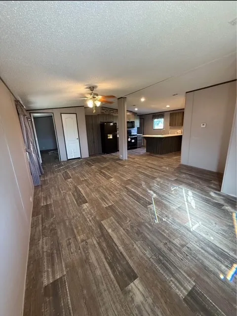 Unfurnished living room with dark wood-style flooring, ceiling fan, and a textured ceiling
