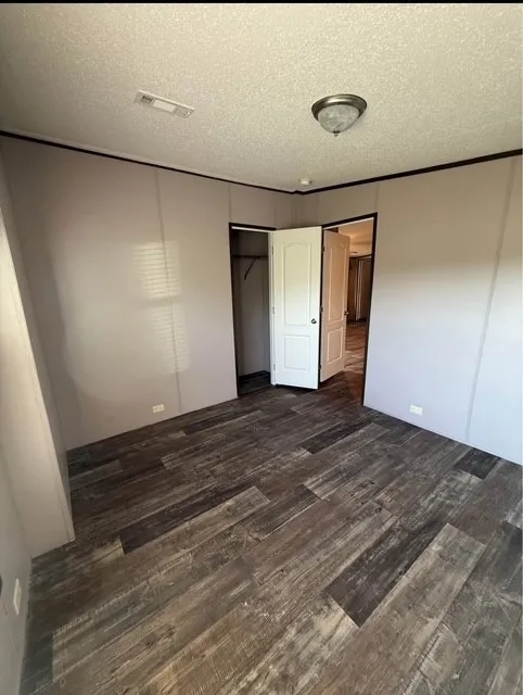 Unfurnished bedroom featuring dark wood-style floors, a closet, and a textured ceiling