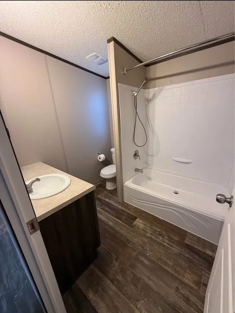 Full bathroom featuring shower / bath combination, dark wood-style floors, vanity, a textured ceiling, and ornamental molding