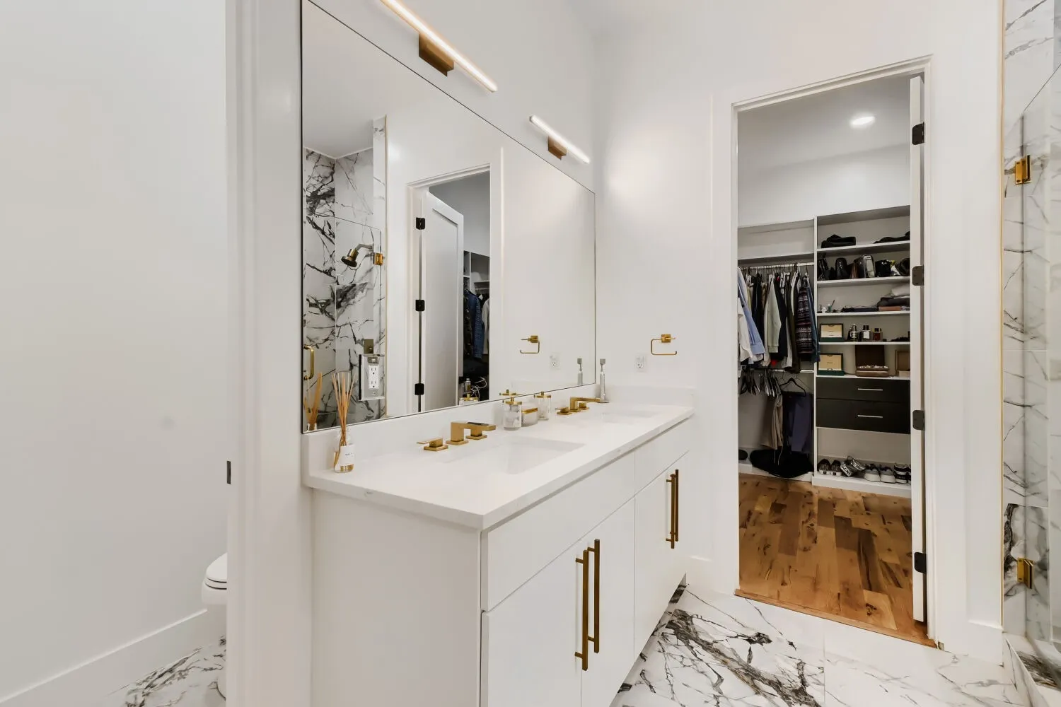 Bathroom featuring double vanity, a walk in closet, light marble finish floors, and a marble finish shower