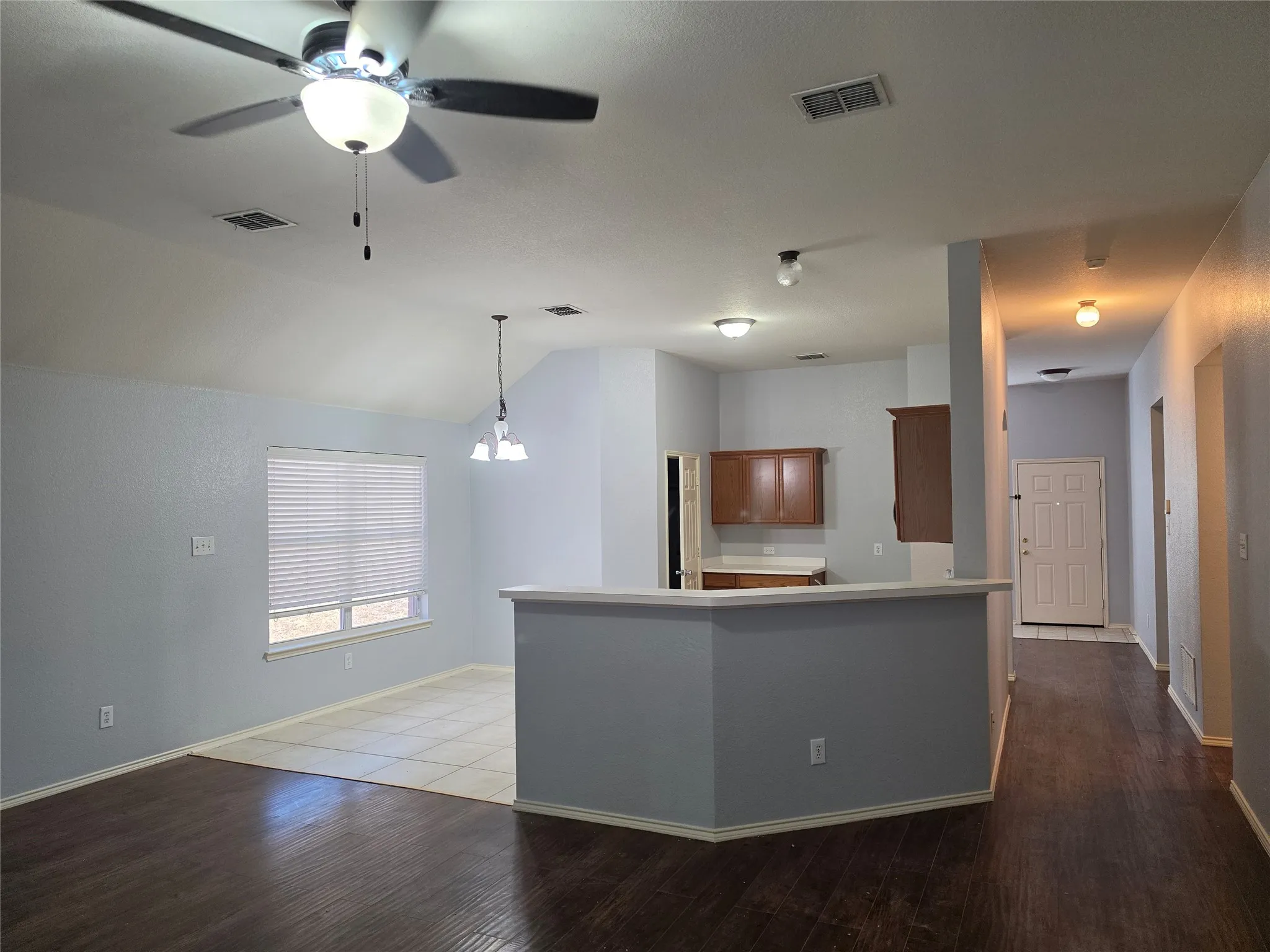 Vaulted ceiling, ceiling fan with light fixture, wood-finish flooring, tiled flooring, and a kitchen pass-through with a breakfast bar