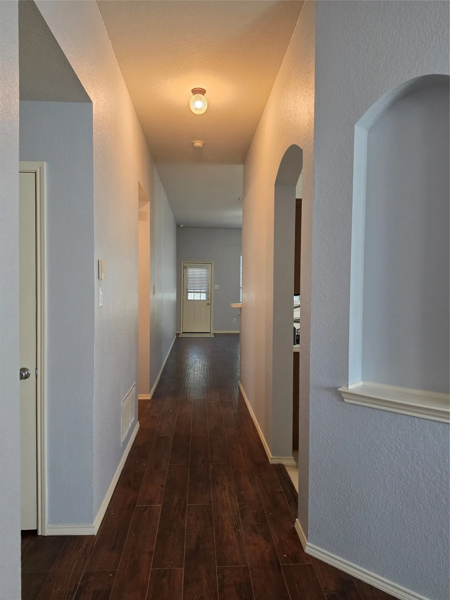Hallway featuring wood-finish flooring, light gray walls, and an arched doorway