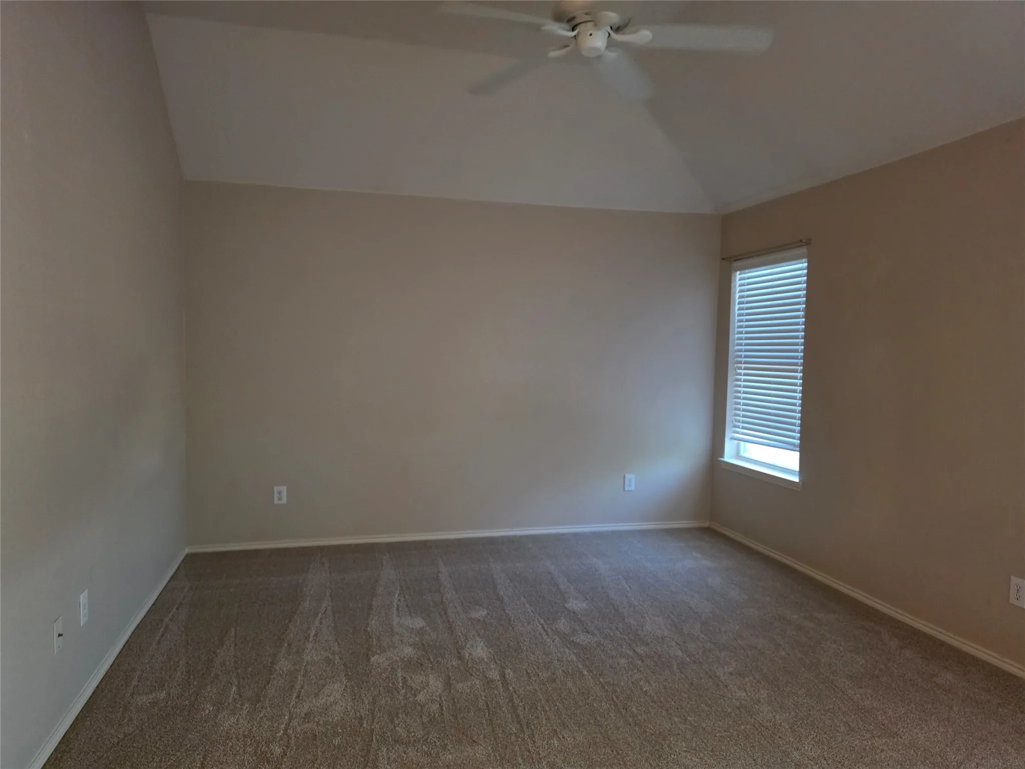 Vaulted ceiling, ceiling fan, carpet flooring, window with blinds, neutral wall paint