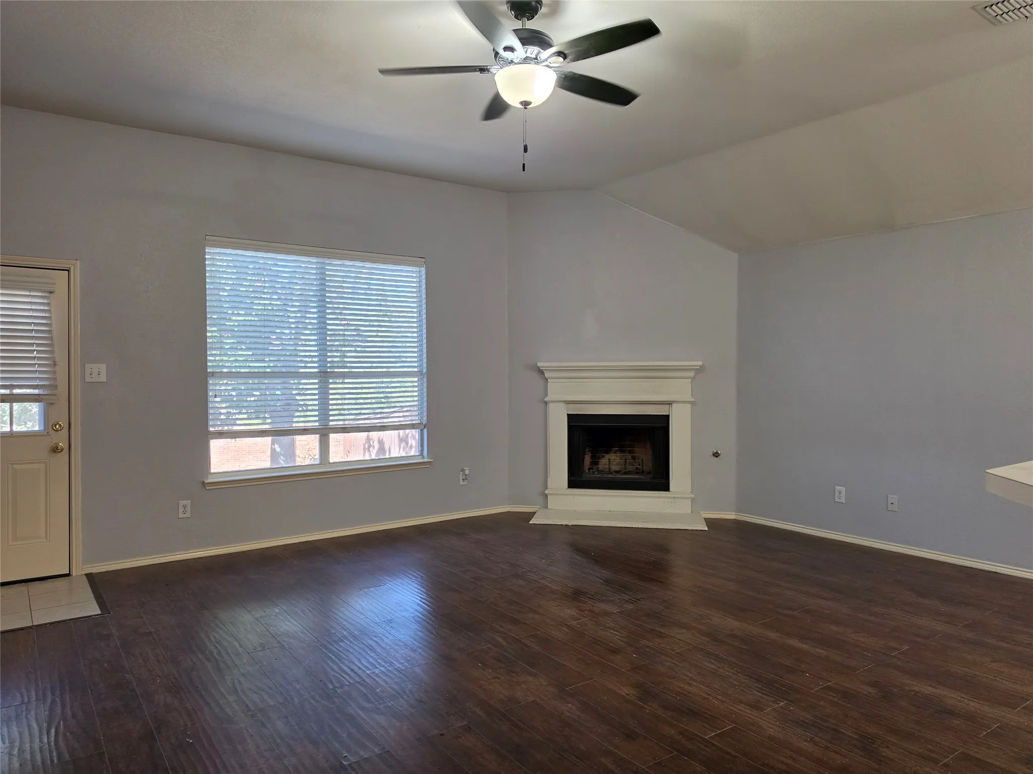 Vaulted ceiling with a ceiling fan, wood-finish flooring, and a fireplace with a white mantel