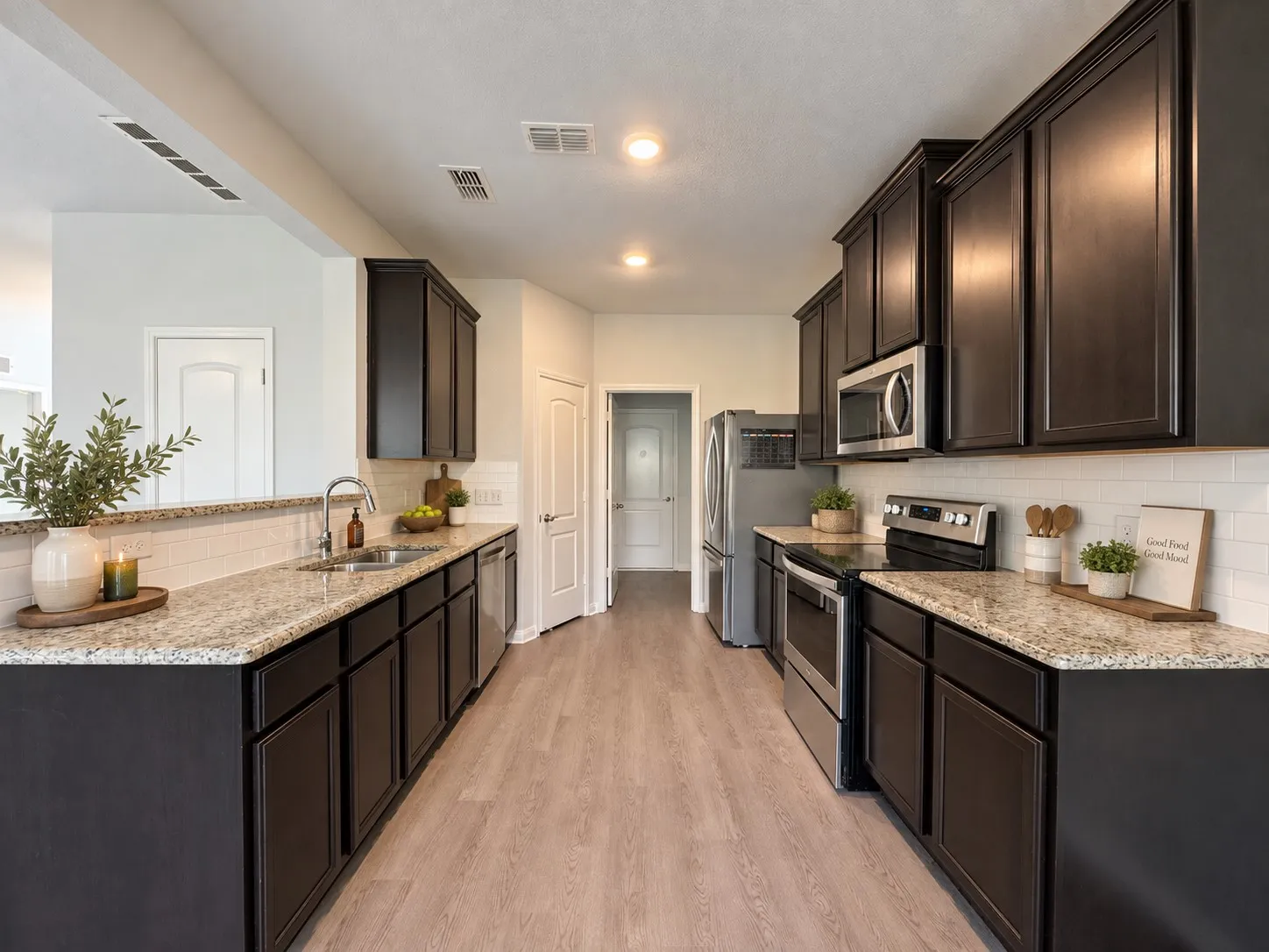 Wood-finish flooring, dark wood cabinetry, light-toned countertops, white subway tile backsplash, and stainless steel appliances