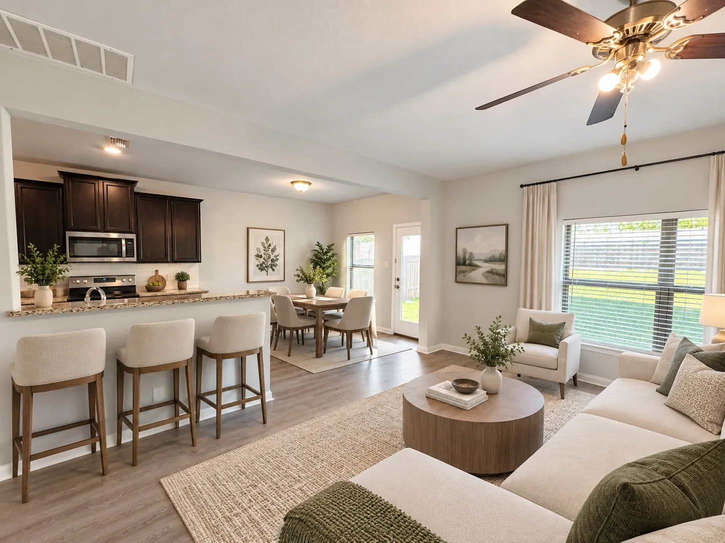 Open-concept living space featuring wood-finish flooring, a kitchen island with stone-finish countertop, dark wood cabinetry, and a ceiling fan with integrated lighting