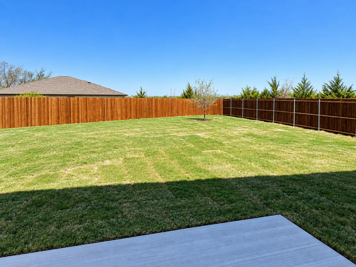 Expansive backyard featuring a lush lawn, privacy fencing, and a concrete patio