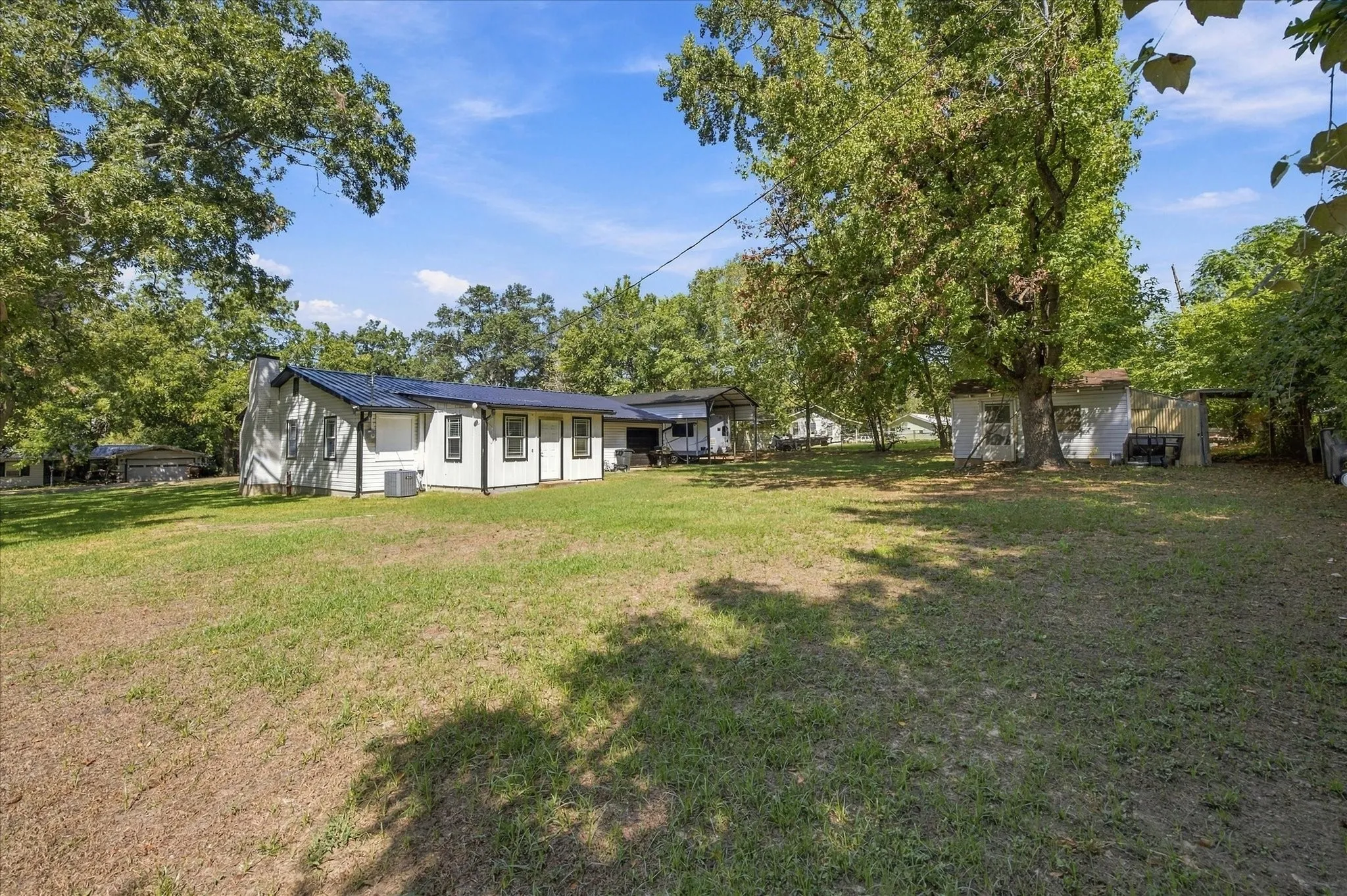 Expansive lawn with mature trees and a white-sided residence featuring dark trim