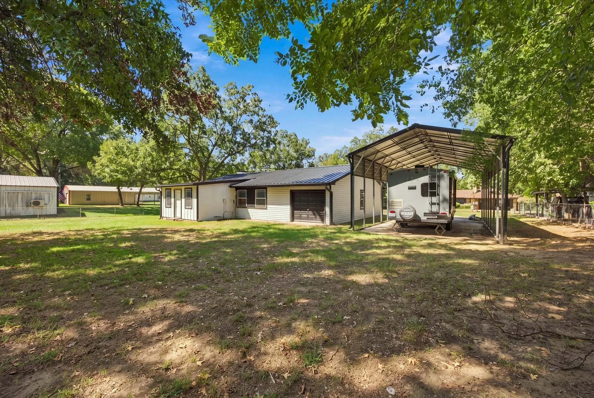 Expansive grass yard with mature trees, a metal carport structure, and a secondary storage building