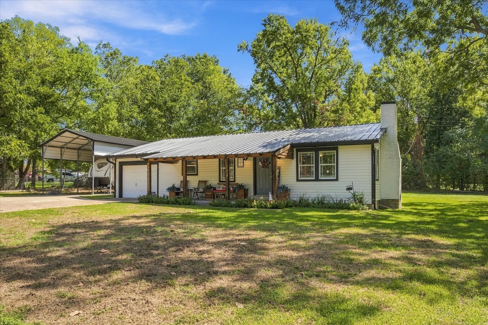 Single-story residence featuring a metal roof, attached garage, covered front porch, and a detached metal carport