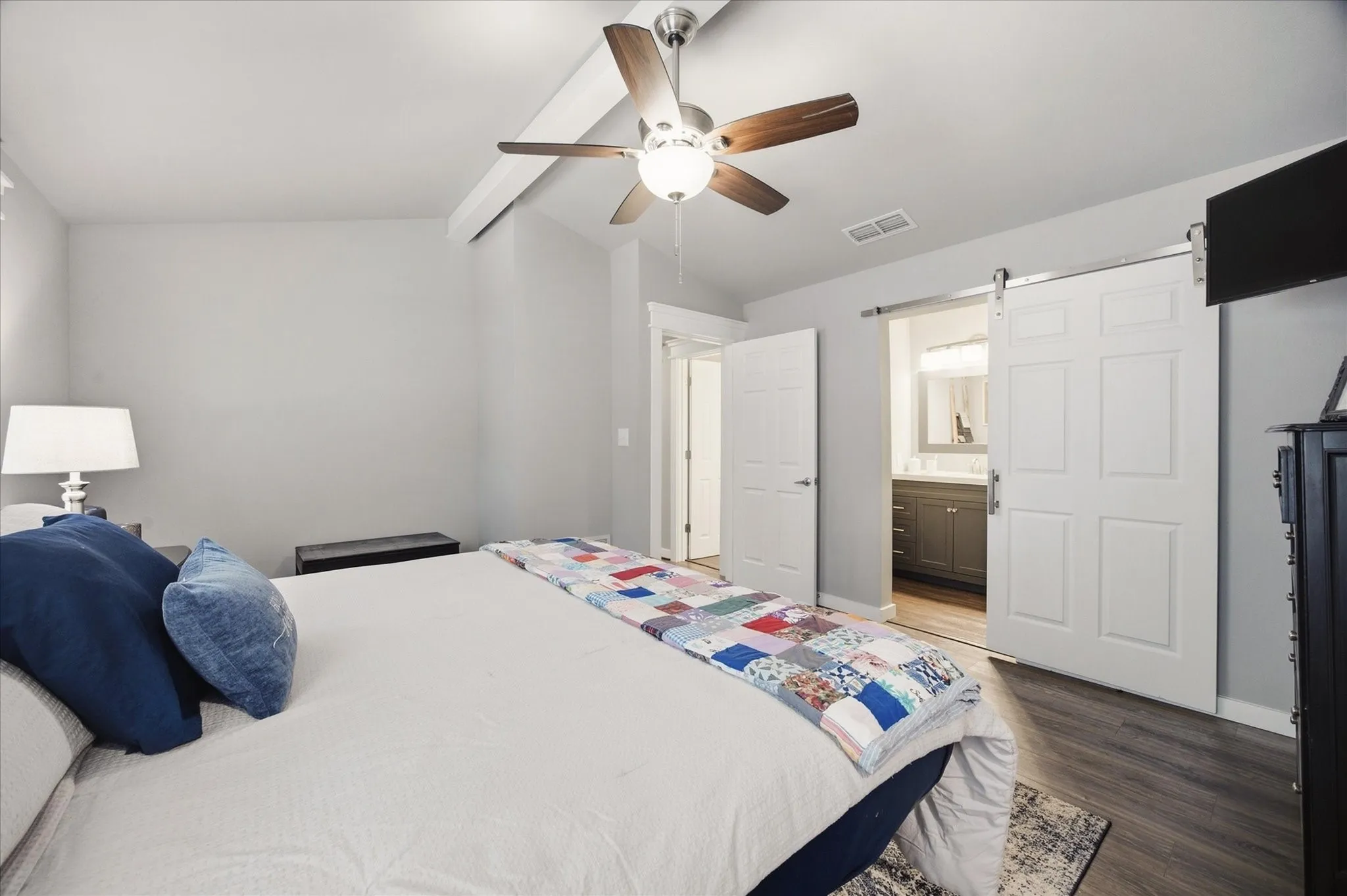 Vaulted ceiling with a ceiling fan, wood-finish flooring, and a white paneled barn door