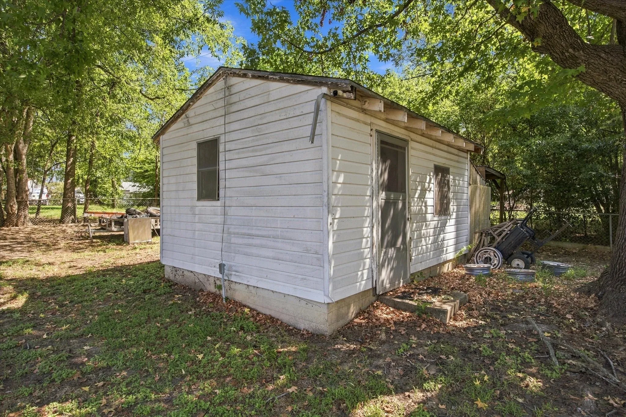 Detached structure with white siding and a concrete foundation, featuring a screened door and two windows