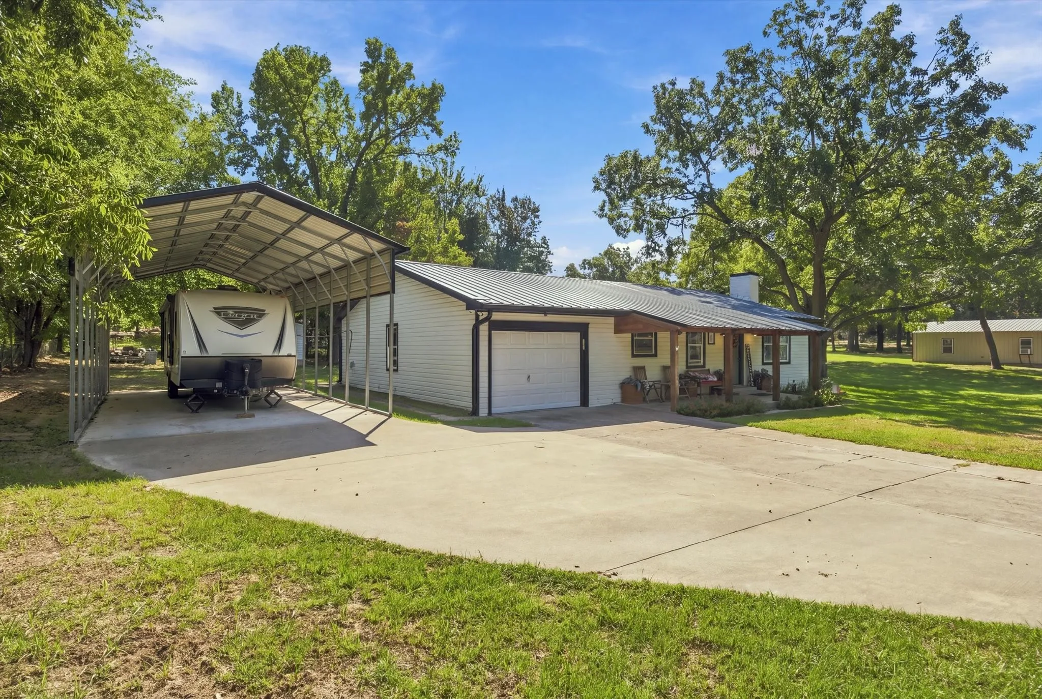 Metal roof residence with a covered front porch, attached garage, and a separate metal carport structure