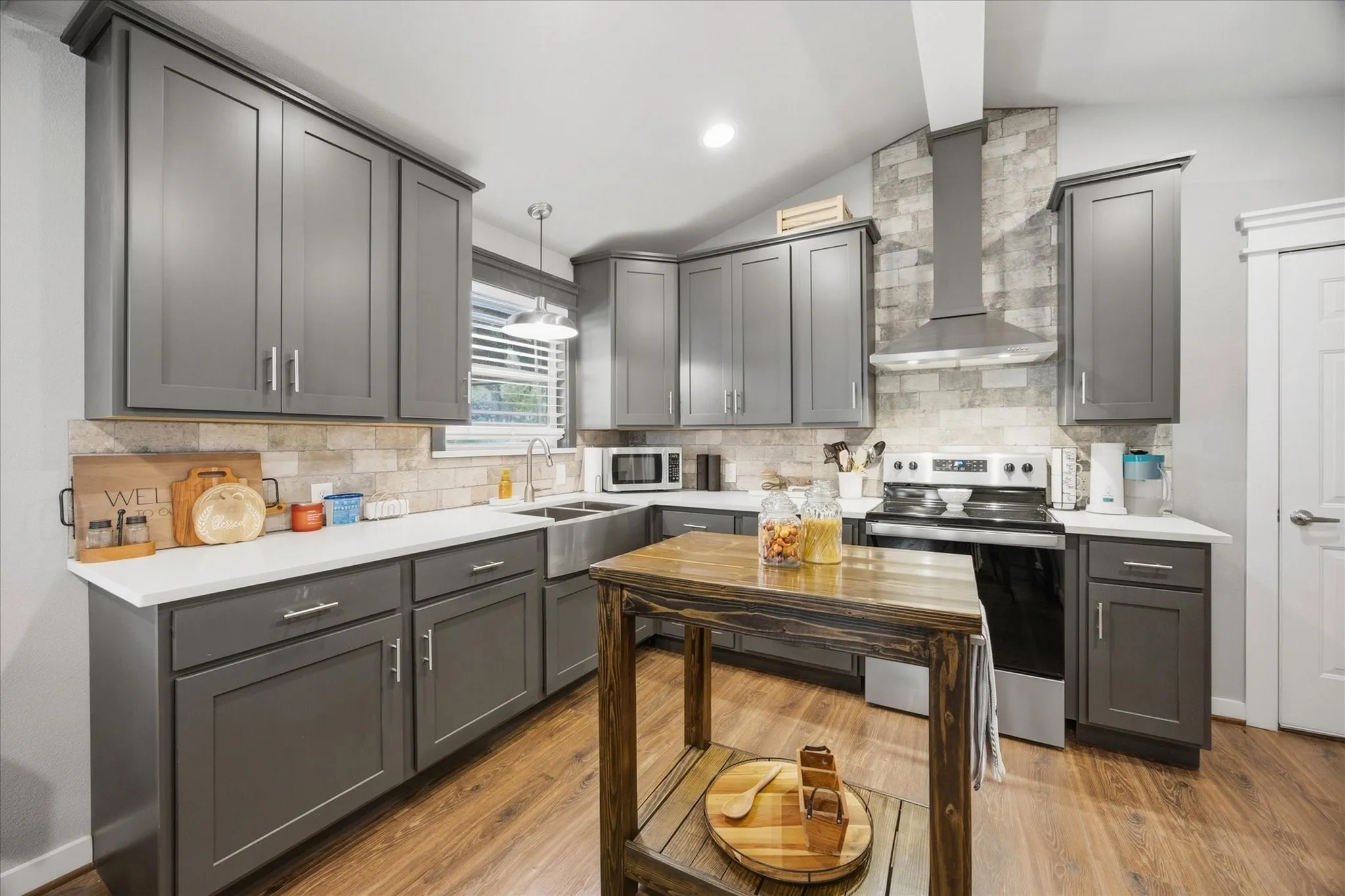 Modern kitchen featuring grey shaker-style cabinetry, white countertops, wood-finish flooring, a stainless steel farmhouse sink, and a tile backsplash