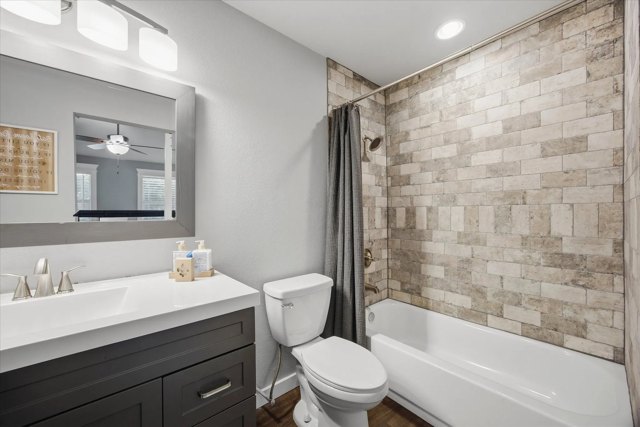 Bathroom featuring a single-sink vanity with white countertop, dark wood-finish cabinetry, brushed nickel faucet, and a shower-tub combination with subway tile surround and bronze fixtures
