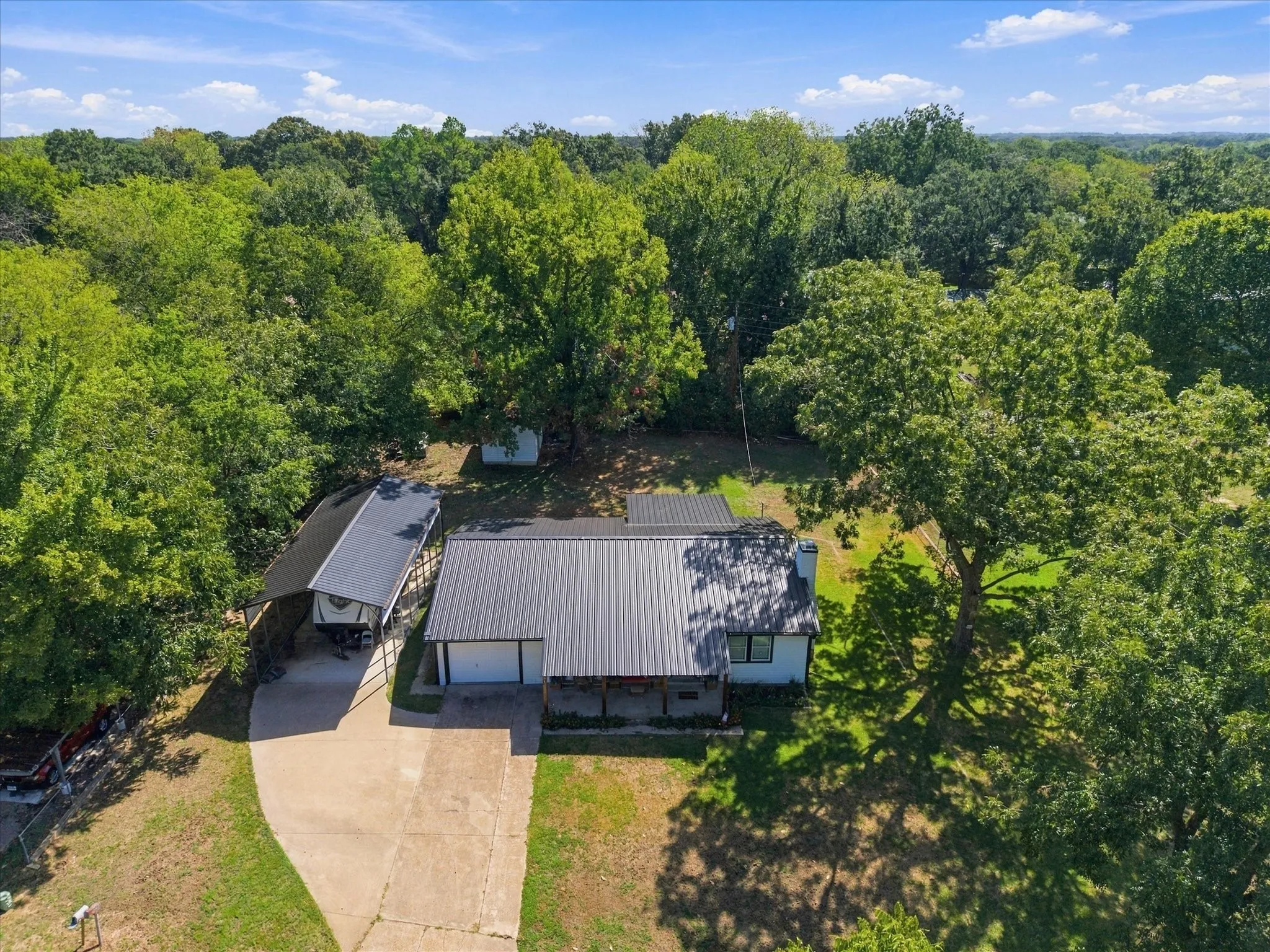 Property featuring a metal roof, attached garage, covered carport, and extensive mature trees