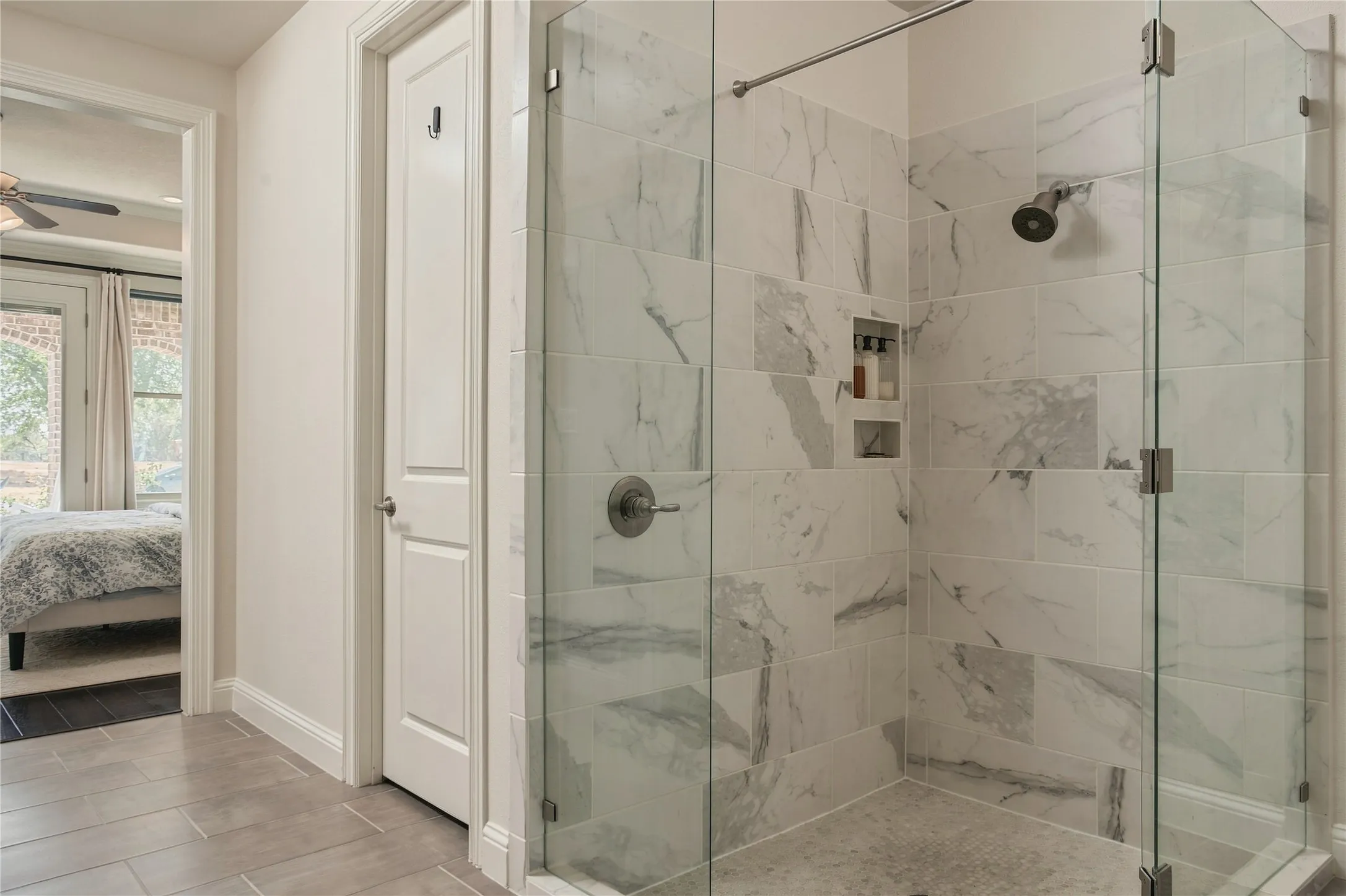 Multiple glass panels keep the oversized shower visually open while showcasing the scale and thoughtful finish of the primary bath. You can see one of the walk-in closets as well. One on each side of the bath's hallway entrance.