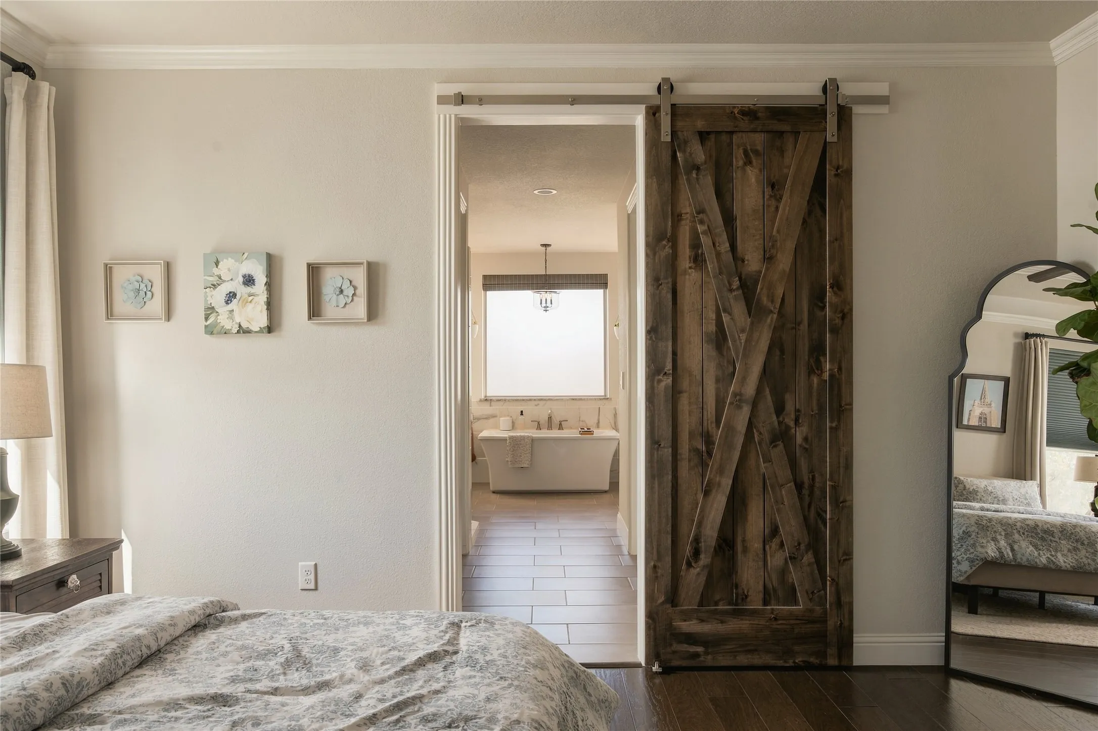 Sliding barn door providing entry to a bathroom featuring a freestanding tub and wood-finish flooring.