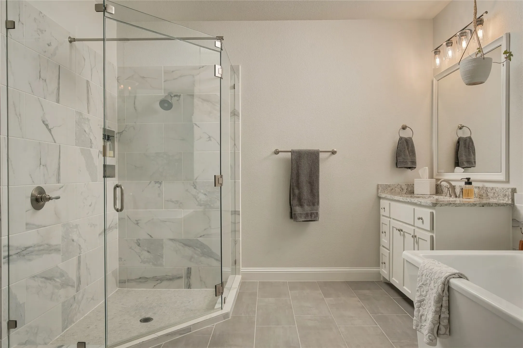 Spa-inspired primary bathroom featuring a frameless glass-enclosed shower with marble tile surround, dual vanity with white cabinetry and stone countertops, freestanding soaking tub, and polished chrome fixtures throughout