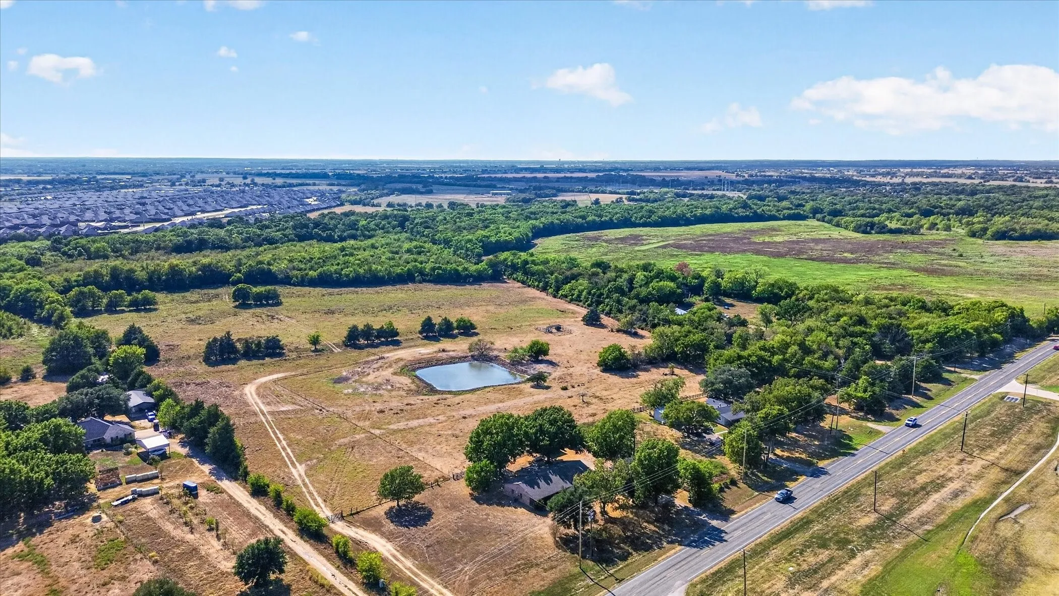 Expansive land parcel featuring a natural pond, a single-story dwelling, and mature tree coverage, bordered by a paved roadway