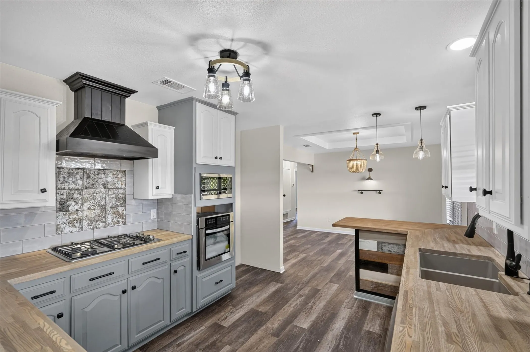 Kitchen featuring wood-finish flooring, two-tone cabinetry, stainless steel appliances, a gas cooktop, and a built-in oven
