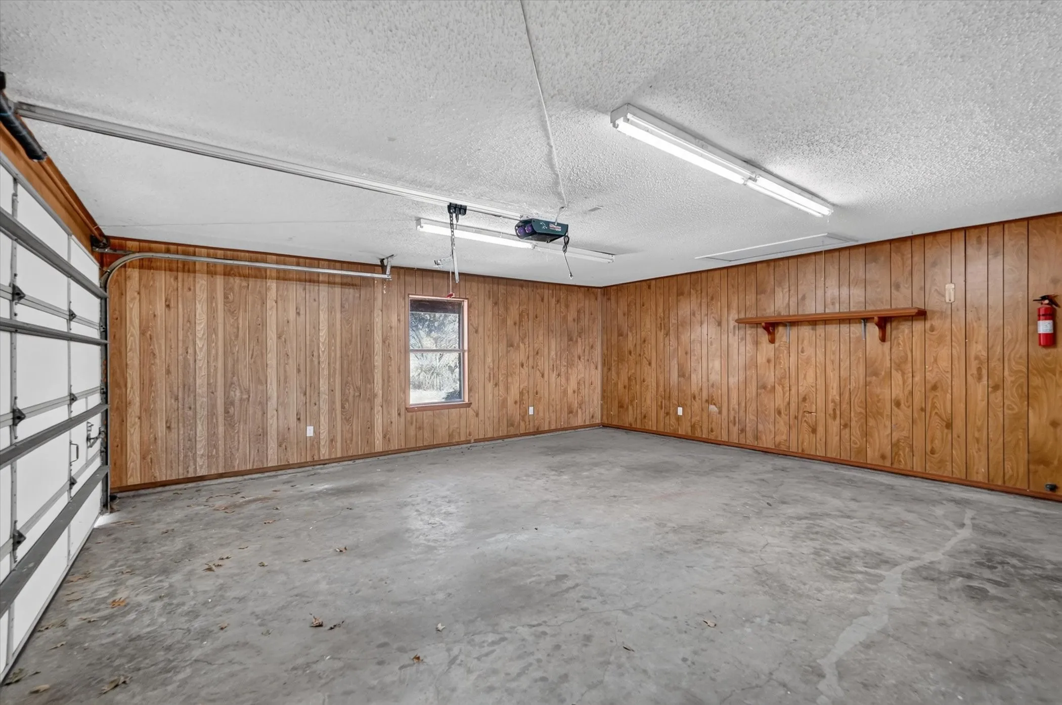 Garage space featuring a roll-up door, concrete flooring, wood-paneled walls, and a built-in window