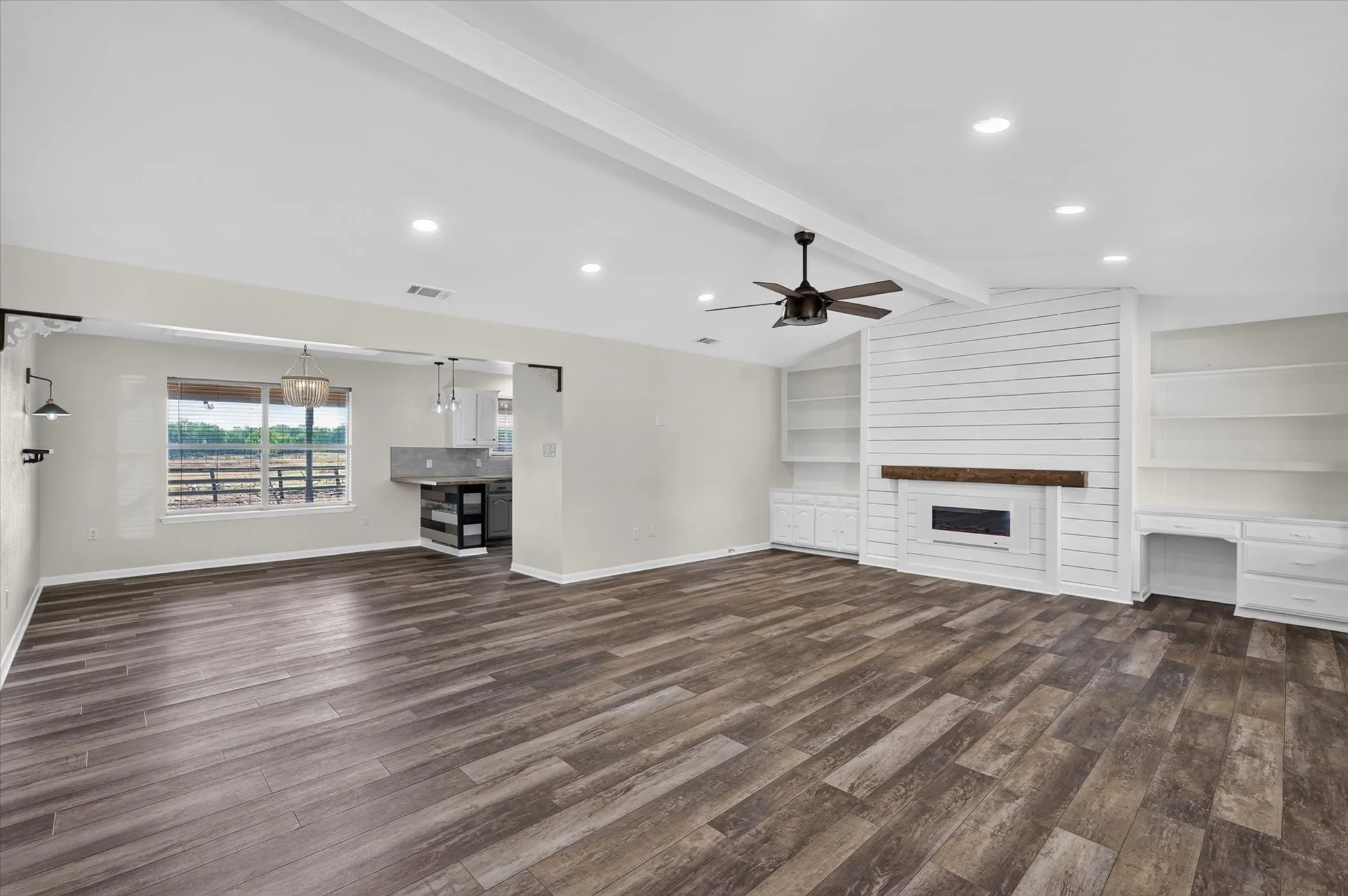 Spacious living area featuring wood-finish flooring, vaulted ceiling with exposed beams, and a modern ceiling fan