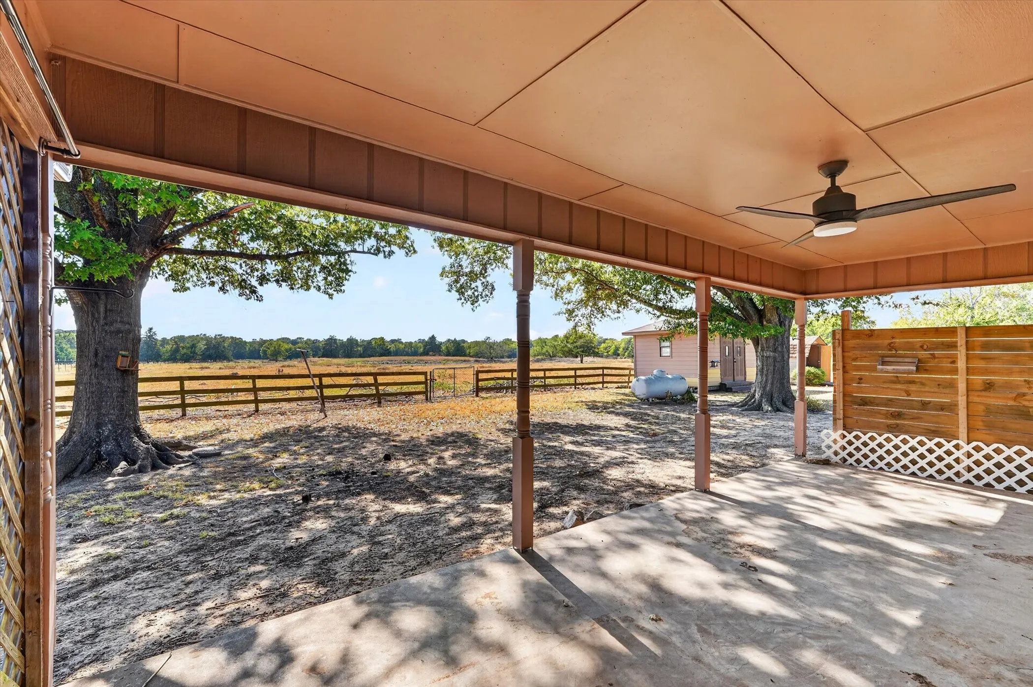 Covered patio with a ceiling fan, exposed wood privacy fence, and concrete flooring