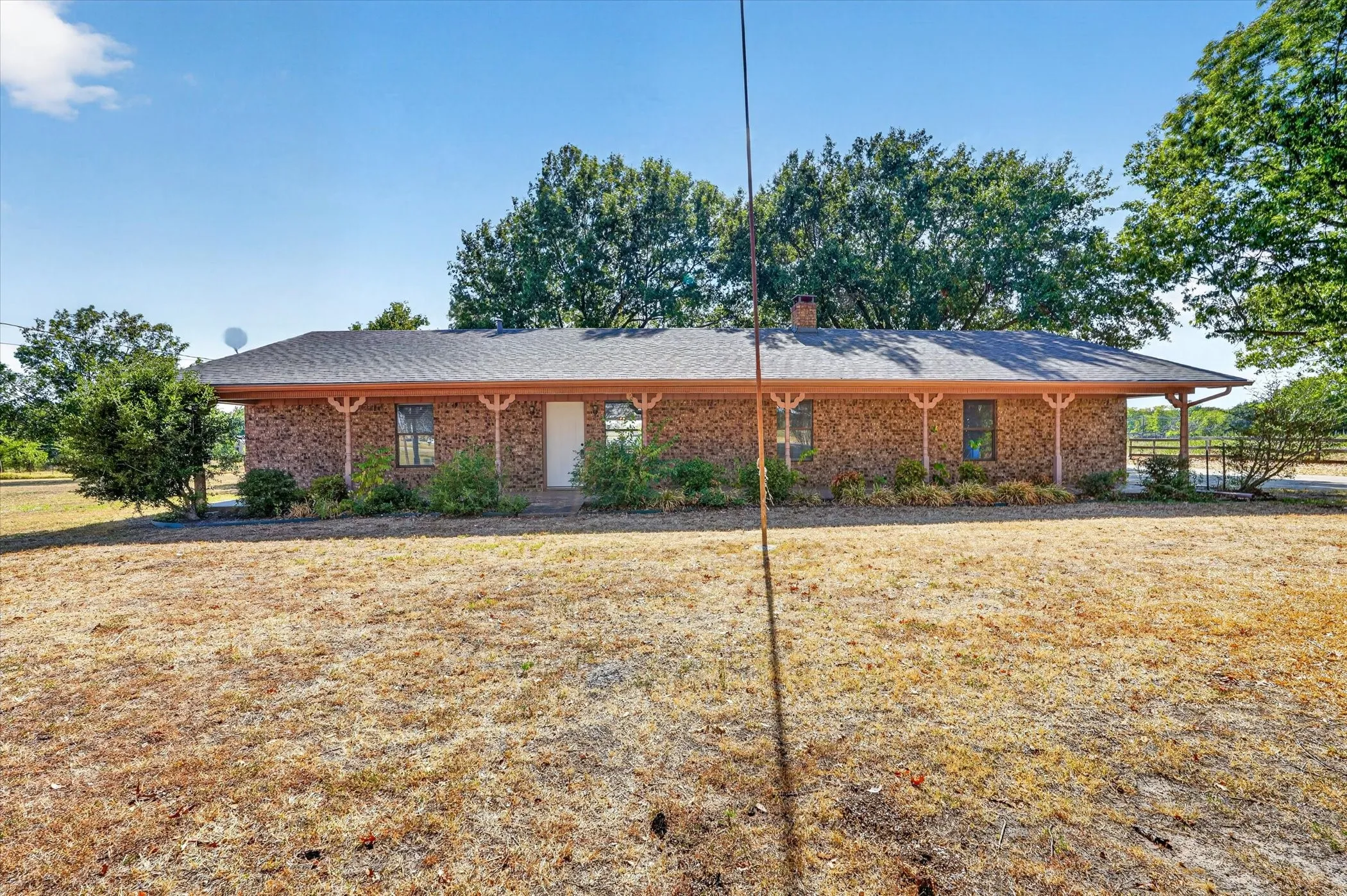 Brick exterior with a shingled roof, covered front porch, and mature landscaping