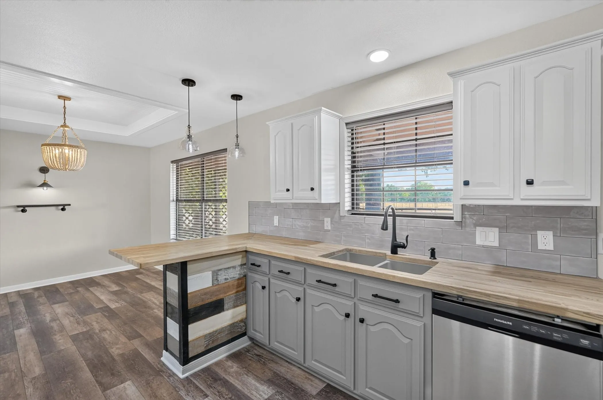 Kitchen with wood-finish flooring, two-tone cabinetry, wood-finish countertops, and subway tile backsplash