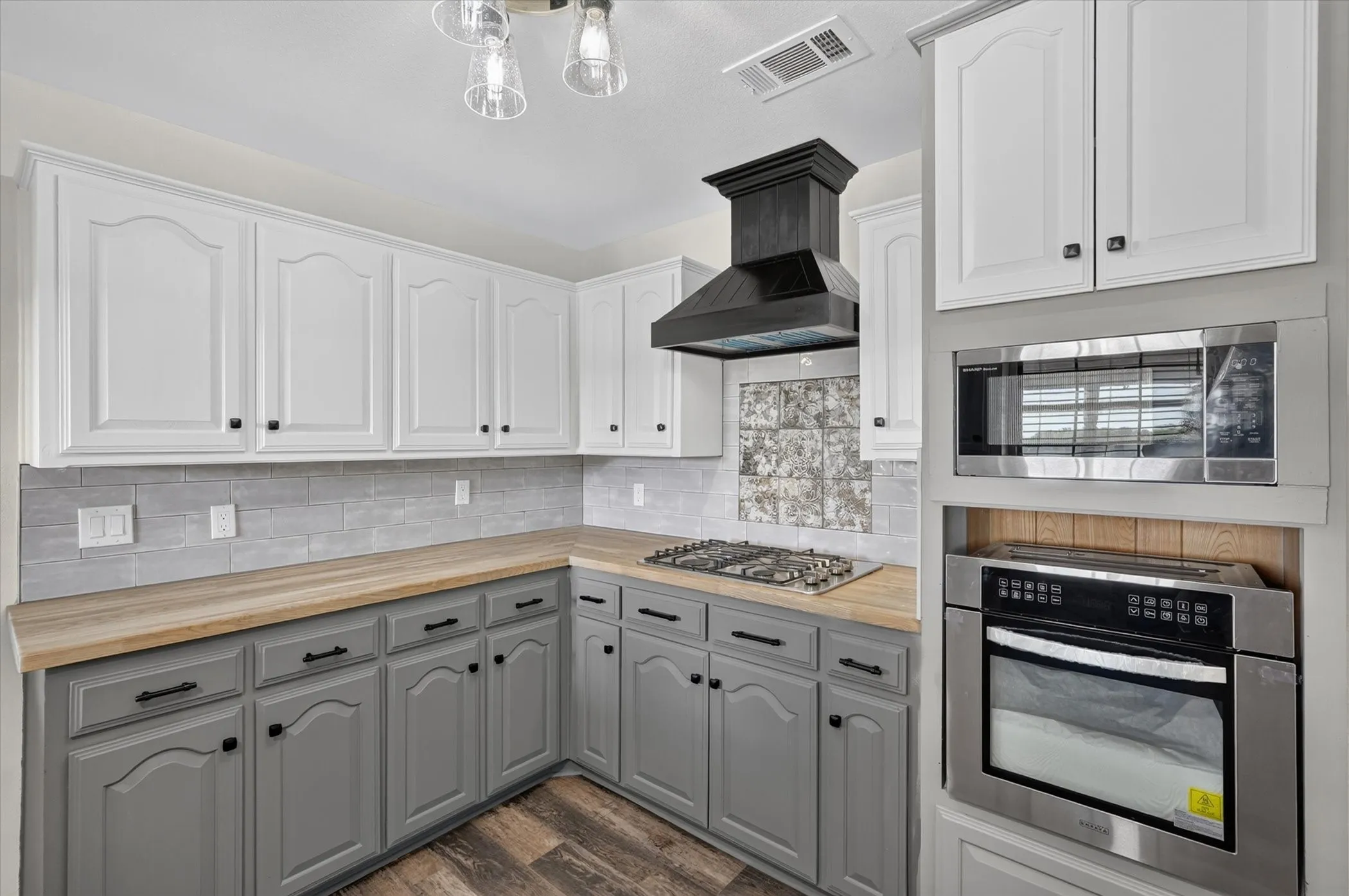 Two-tone cabinetry with light wood-finish countertops, stainless steel appliances, a gas cooktop, and a decorative range hood