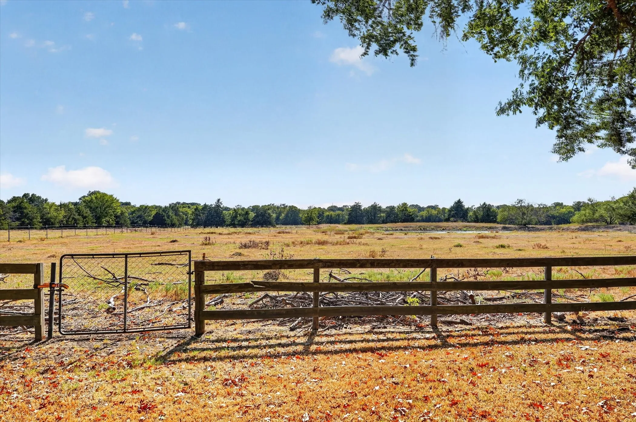 Expansive cleared land featuring a natural wood fence and a metal gate