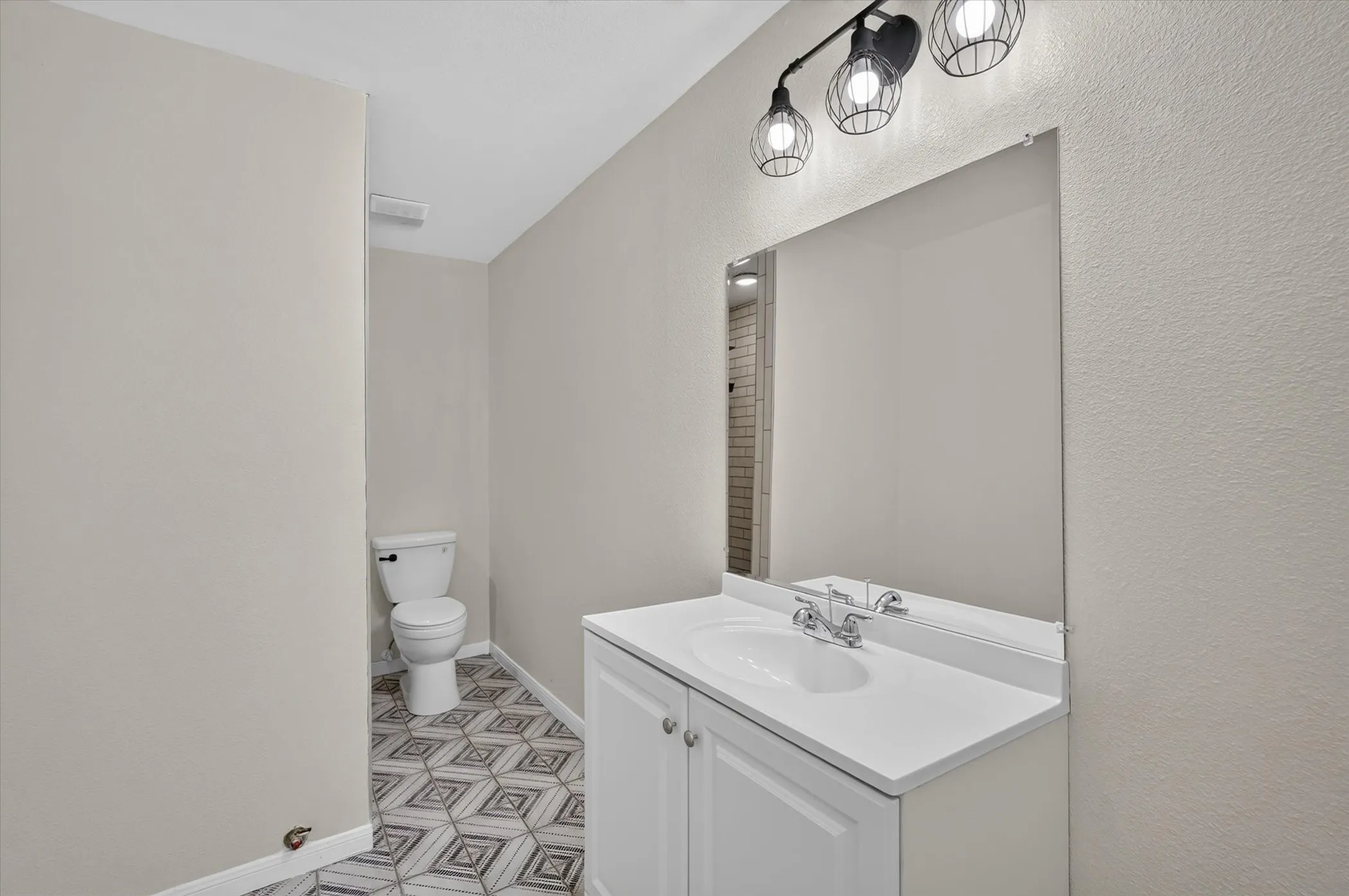 Vanity with an integrated sink and chrome faucet, large wall mirror, and modern three-light fixture