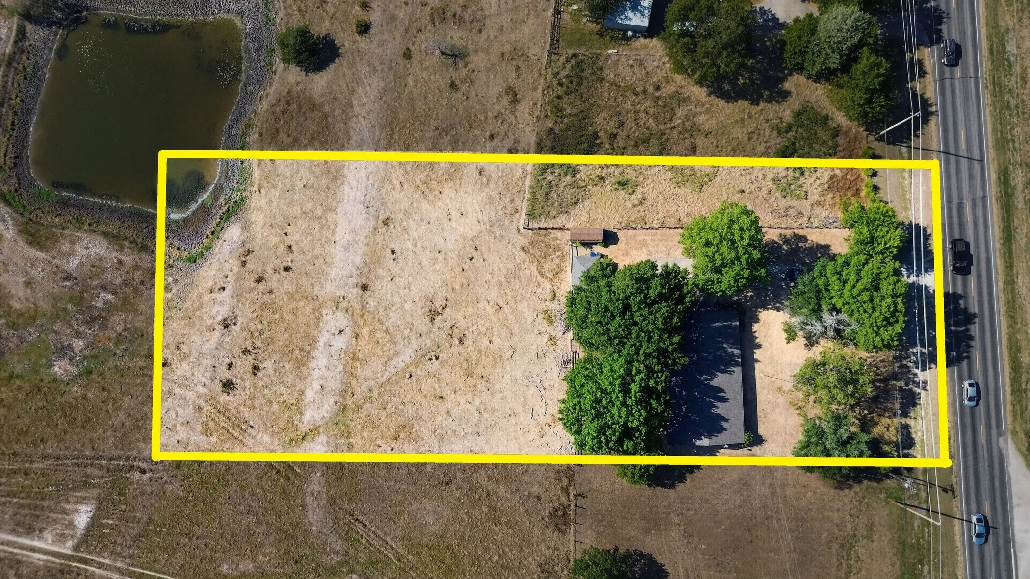Expansive lot featuring a residential structure, mature trees, and a roadside location