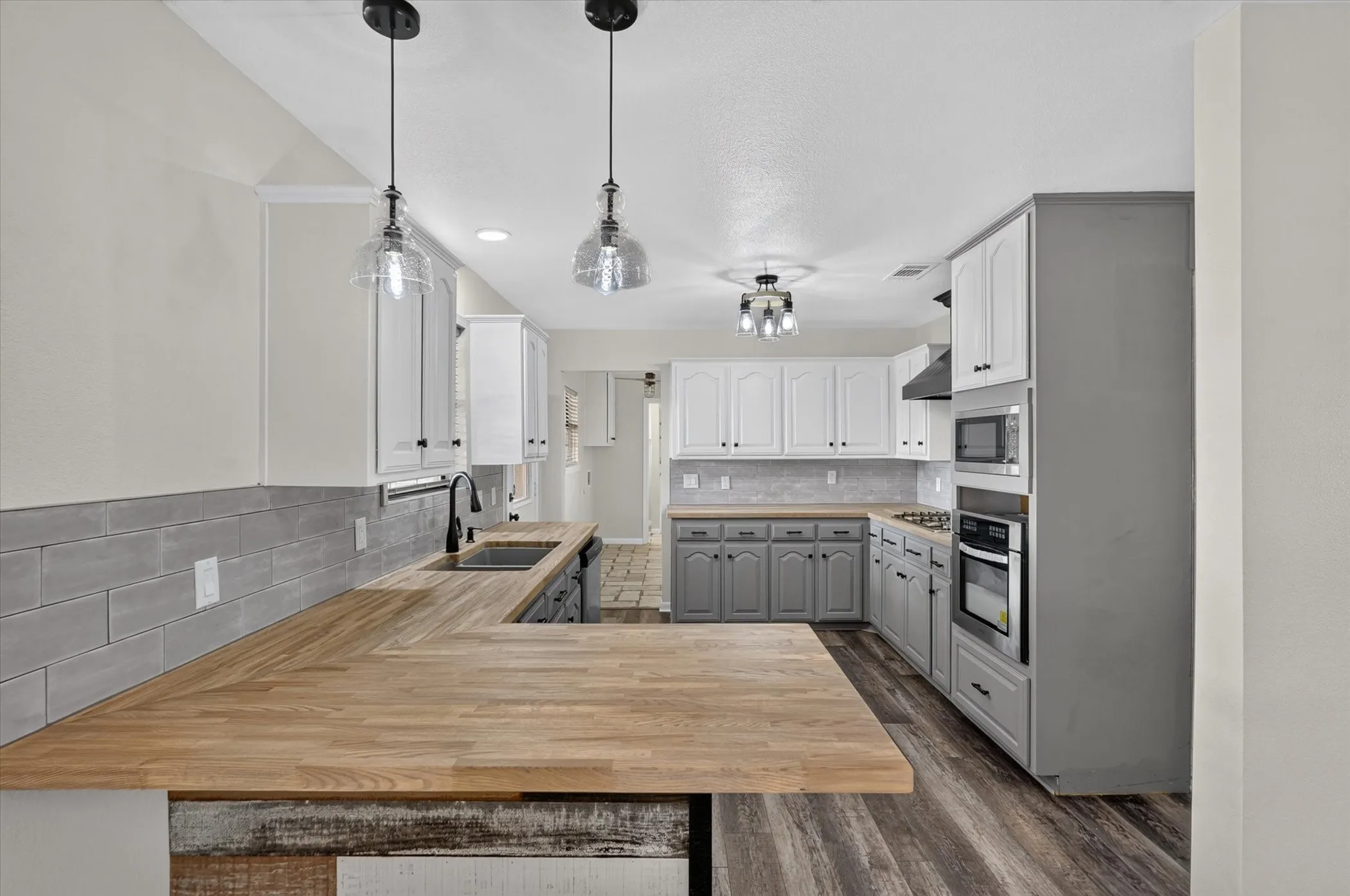 Kitchen featuring wood-finish countertops, two-tone cabinetry, stainless steel appliances, a tile backsplash, and a built-in cooktop