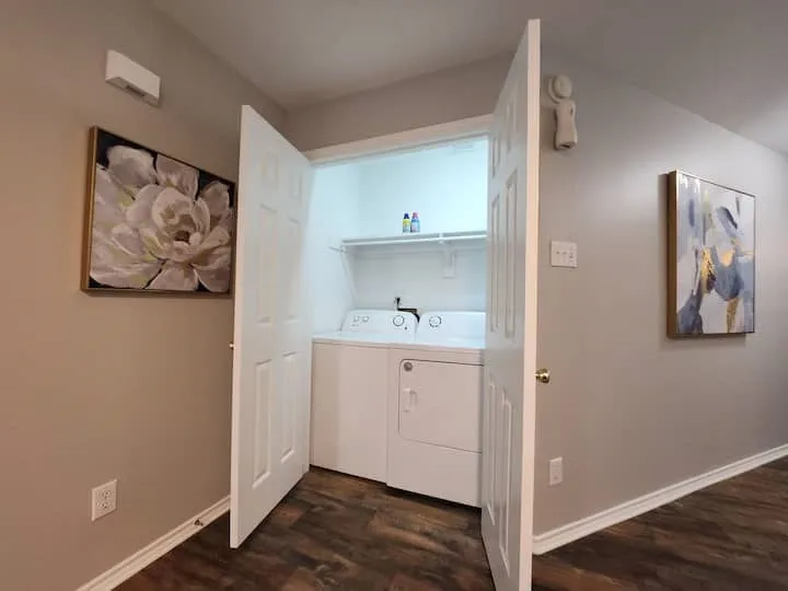 Laundry closet with white bi-fold doors, white stacked appliances, and wood-finish flooring
