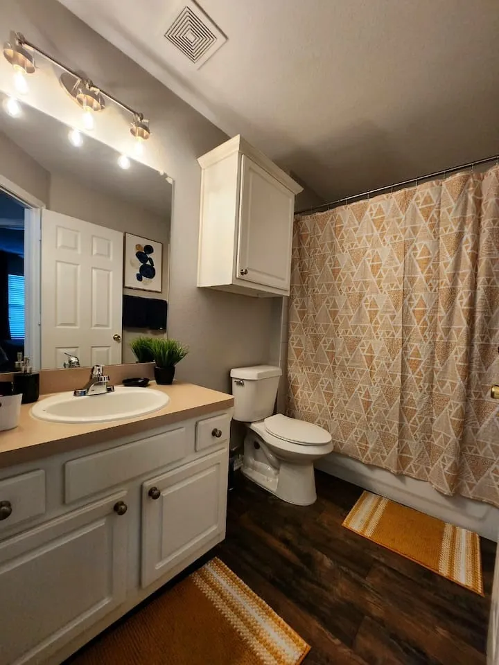 Vanity with an integrated sink, wood-finish flooring, built-in upper cabinetry, and a full bathtub with a shower
