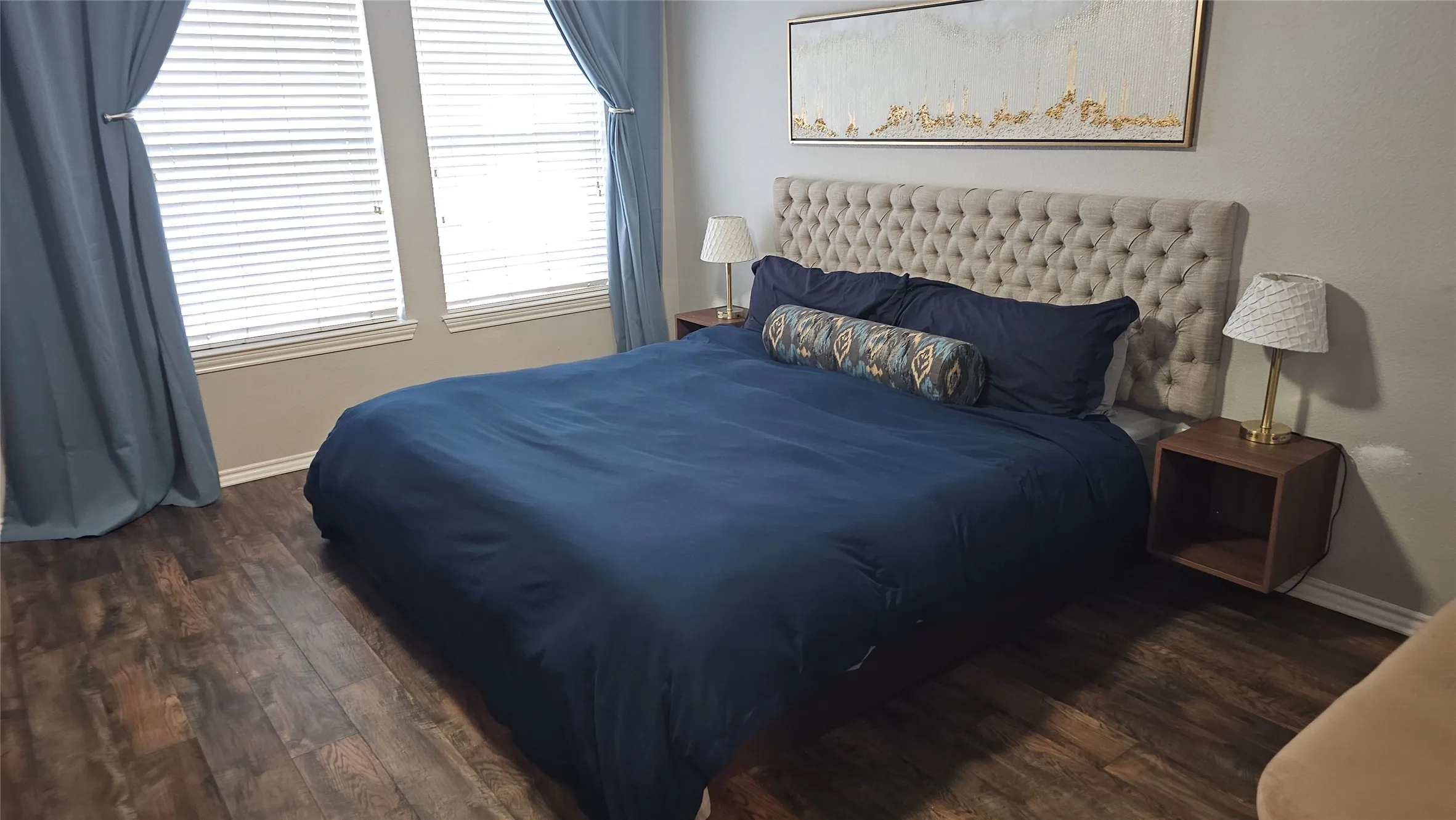 Wood-finish flooring, two windows with blinds, and a tufted upholstered headboard