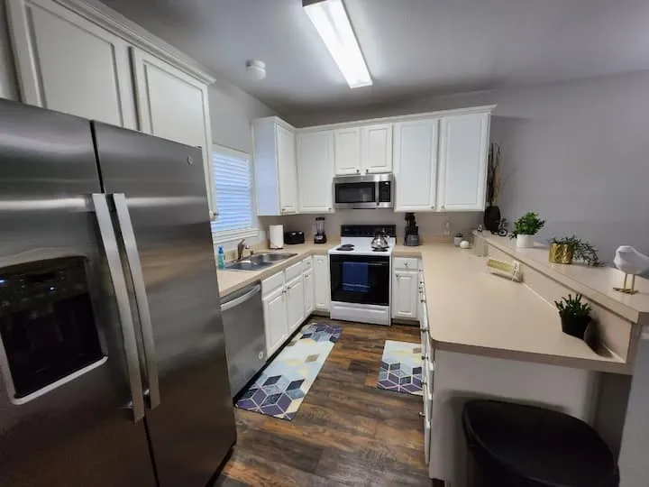 Kitchen featuring wood-finish flooring, white cabinetry, stainless steel appliances, and a raised countertop