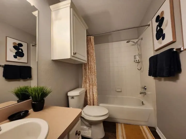White ceramic bathtub with a shower attachment, white subway tile surround, white toilet, and white vanity cabinetry with a light-colored countertop