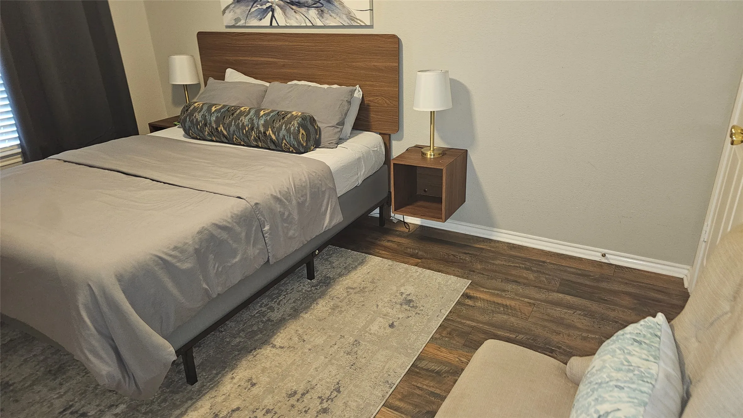 Wood-finish flooring, light neutral wall paint, and a wood-finish headboard