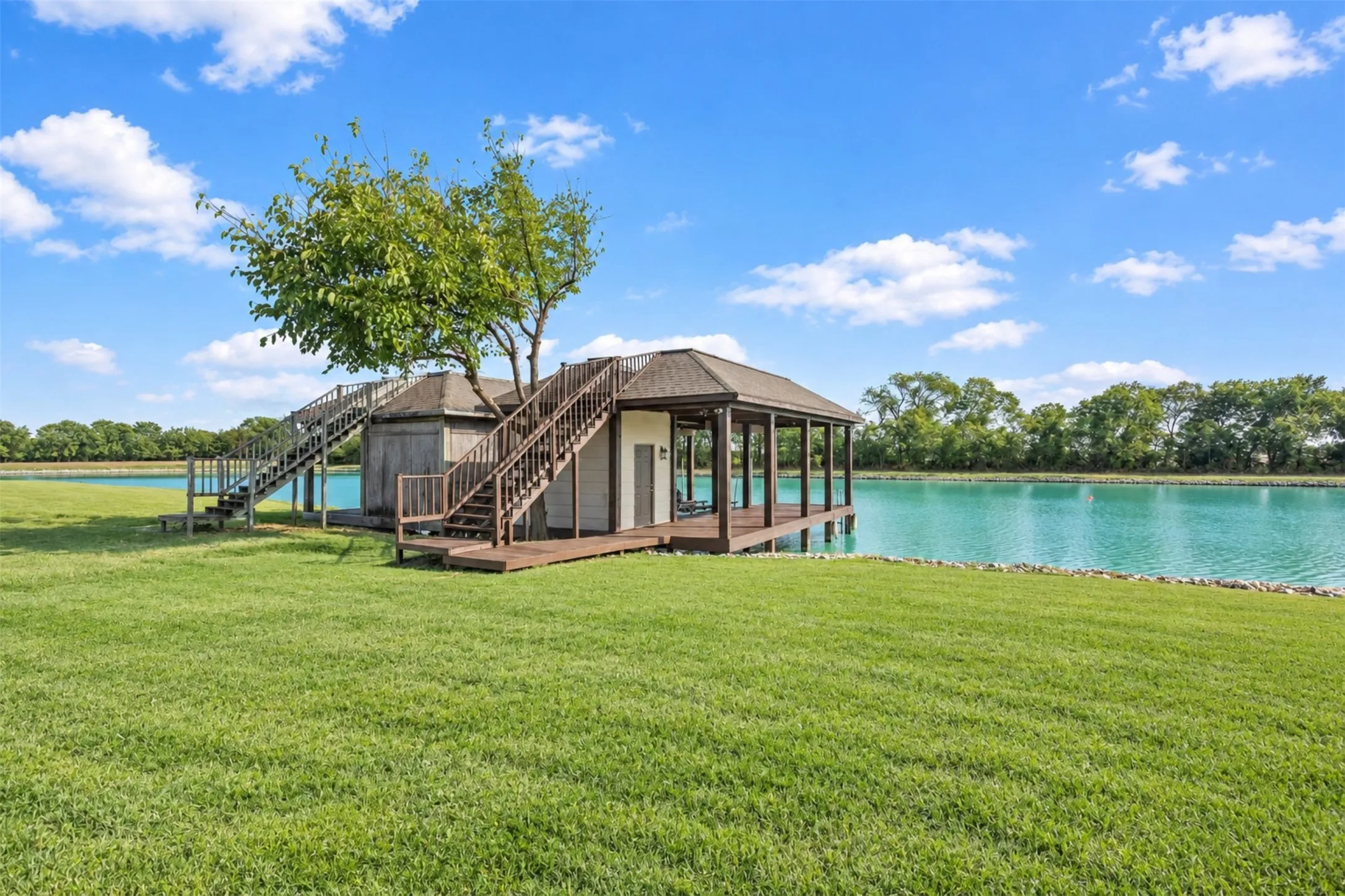 Expansive grassy area with a waterside gazebo, a boathouse, and an additional covered structure