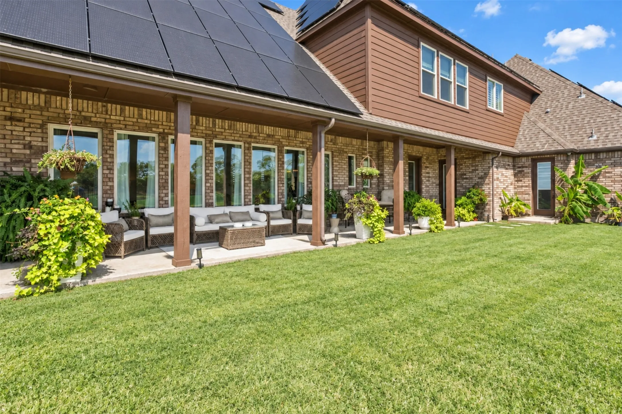 Expansive green lawn with a covered patio featuring wood-finish columns and multiple windows