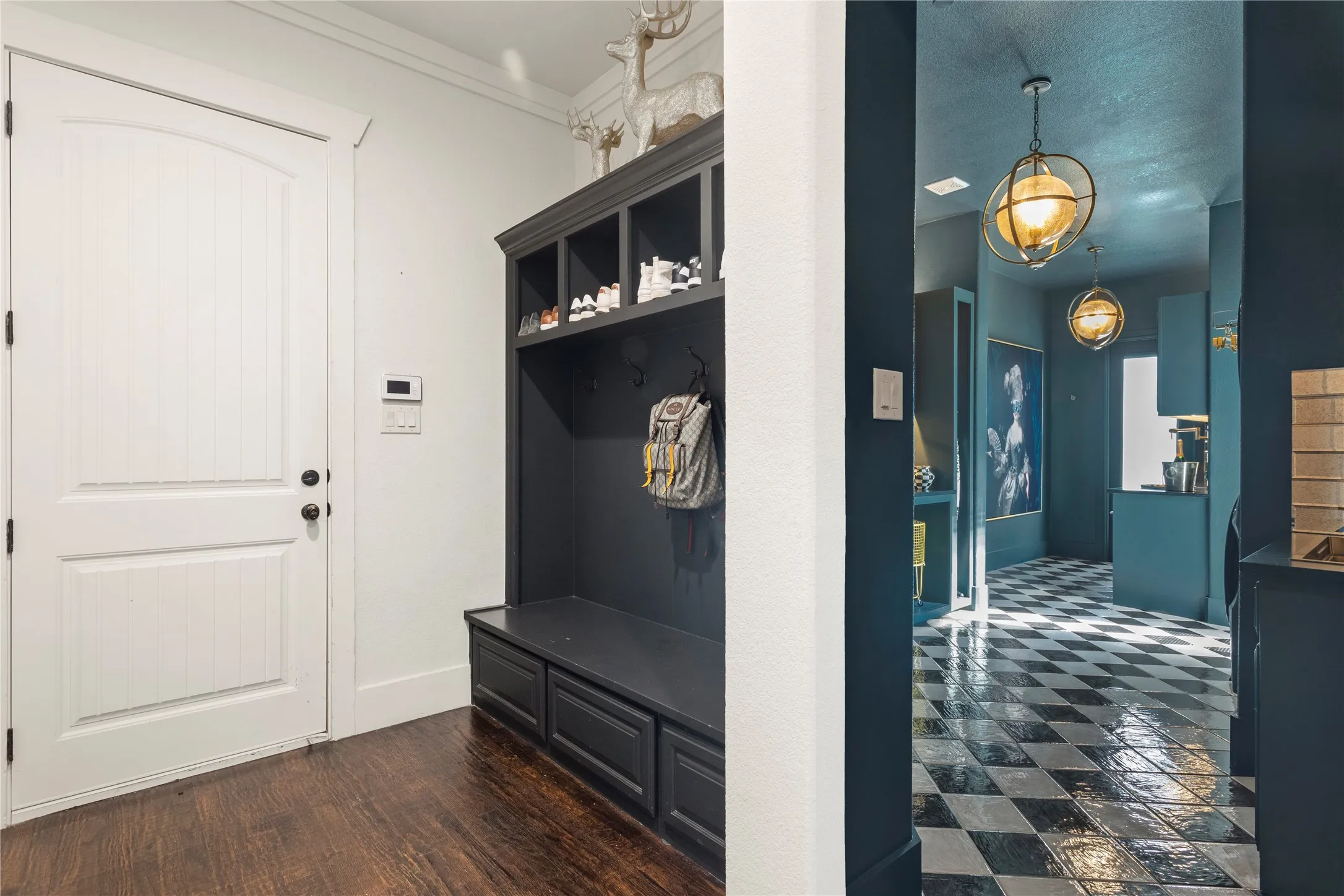 Built-in hall tree with integrated storage and seating, hardwood flooring, arched panel door, and checkered tile flooring in the hallway