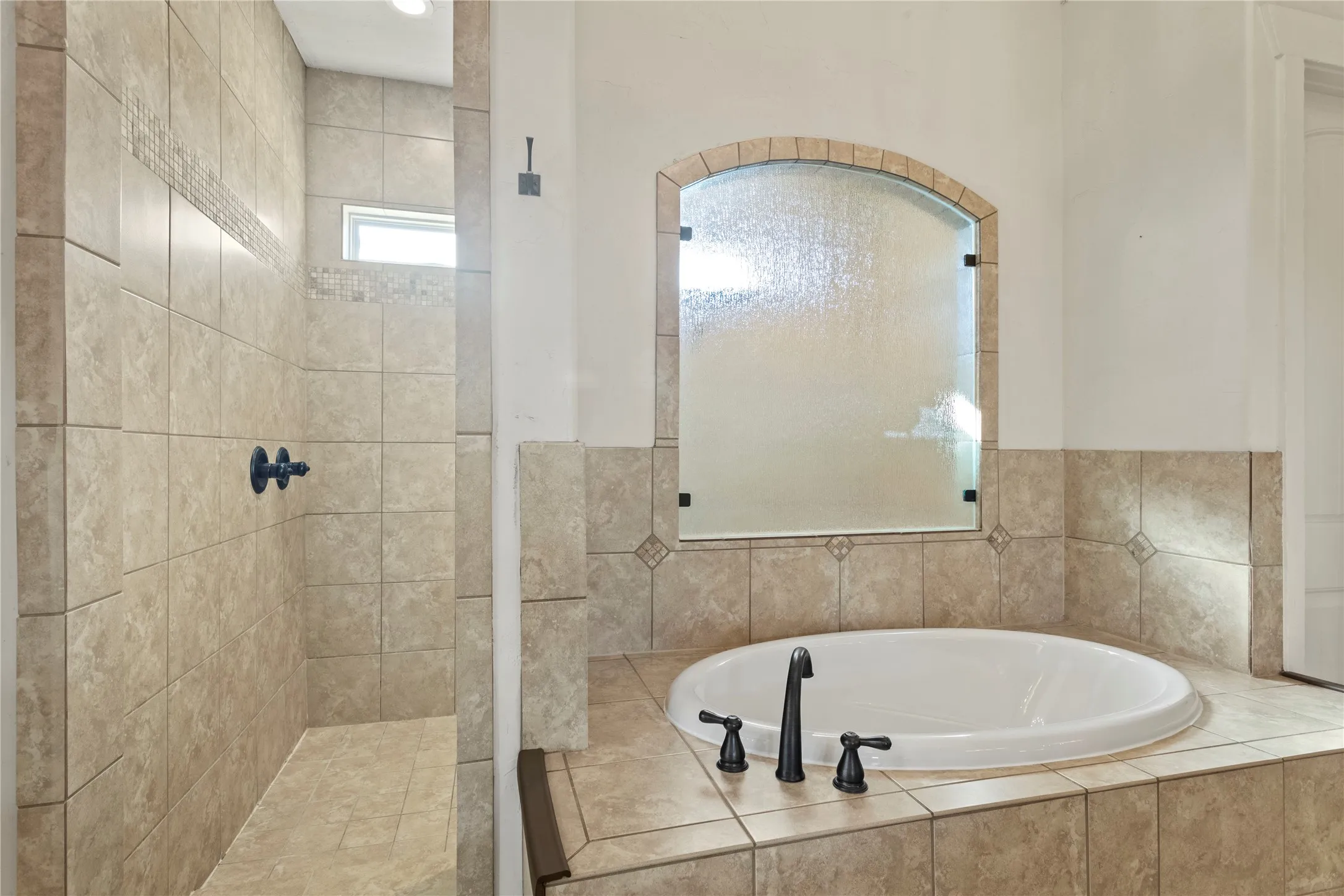 Tiled shower with a transom window, an arched frosted glass partition, a built-in soaking tub, and oil-rubbed bronze fixtures