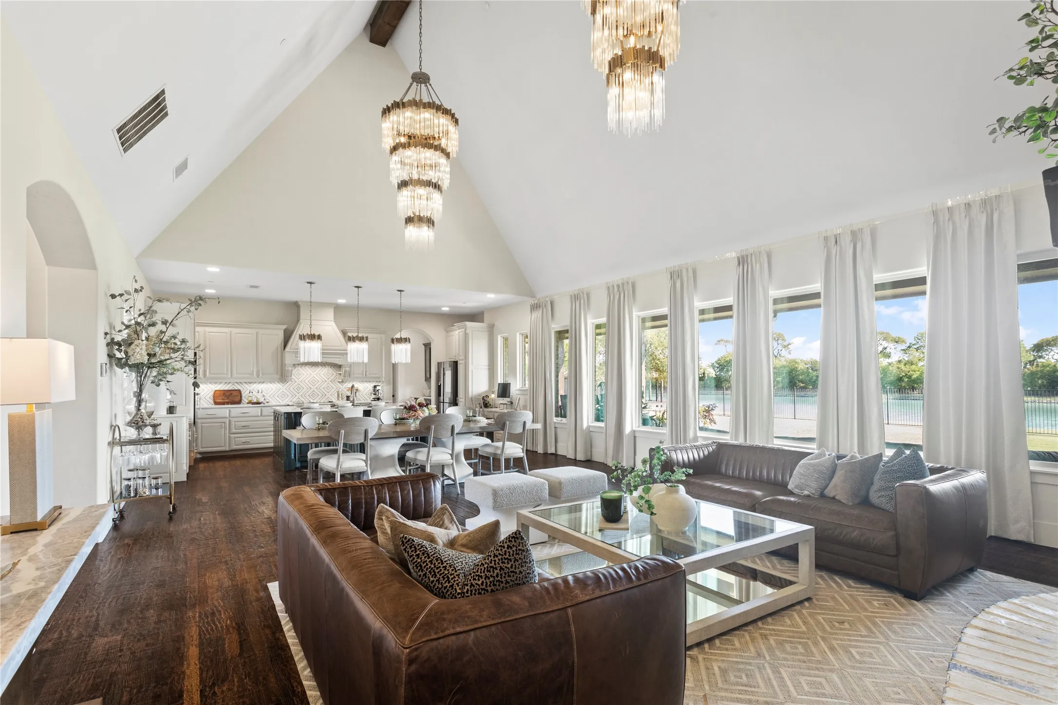 Vaulted ceilings, wood-finish flooring, multiple tiered chandeliers, a full wall of windows, and built-in kitchen cabinetry