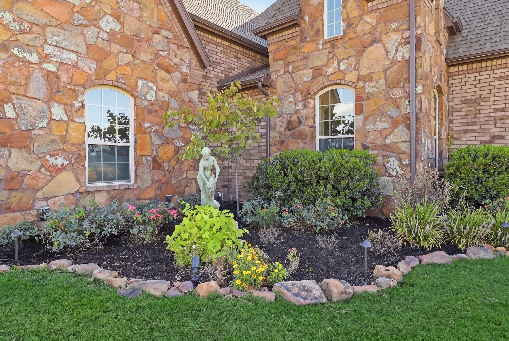 Stone and brick exterior with arched windows, manicured landscaping, and a stone-edged garden bed