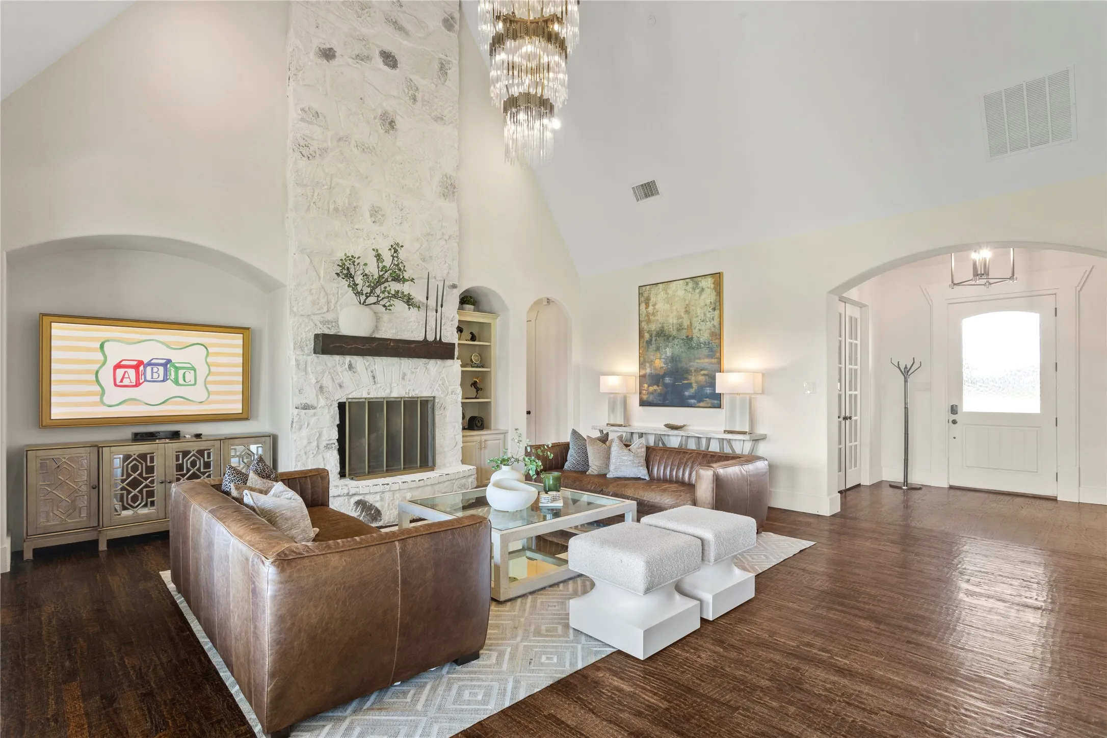 Vaulted ceiling, stone fireplace with a wood mantel, dark wood-finish flooring, arched doorways, and a contemporary chandelier